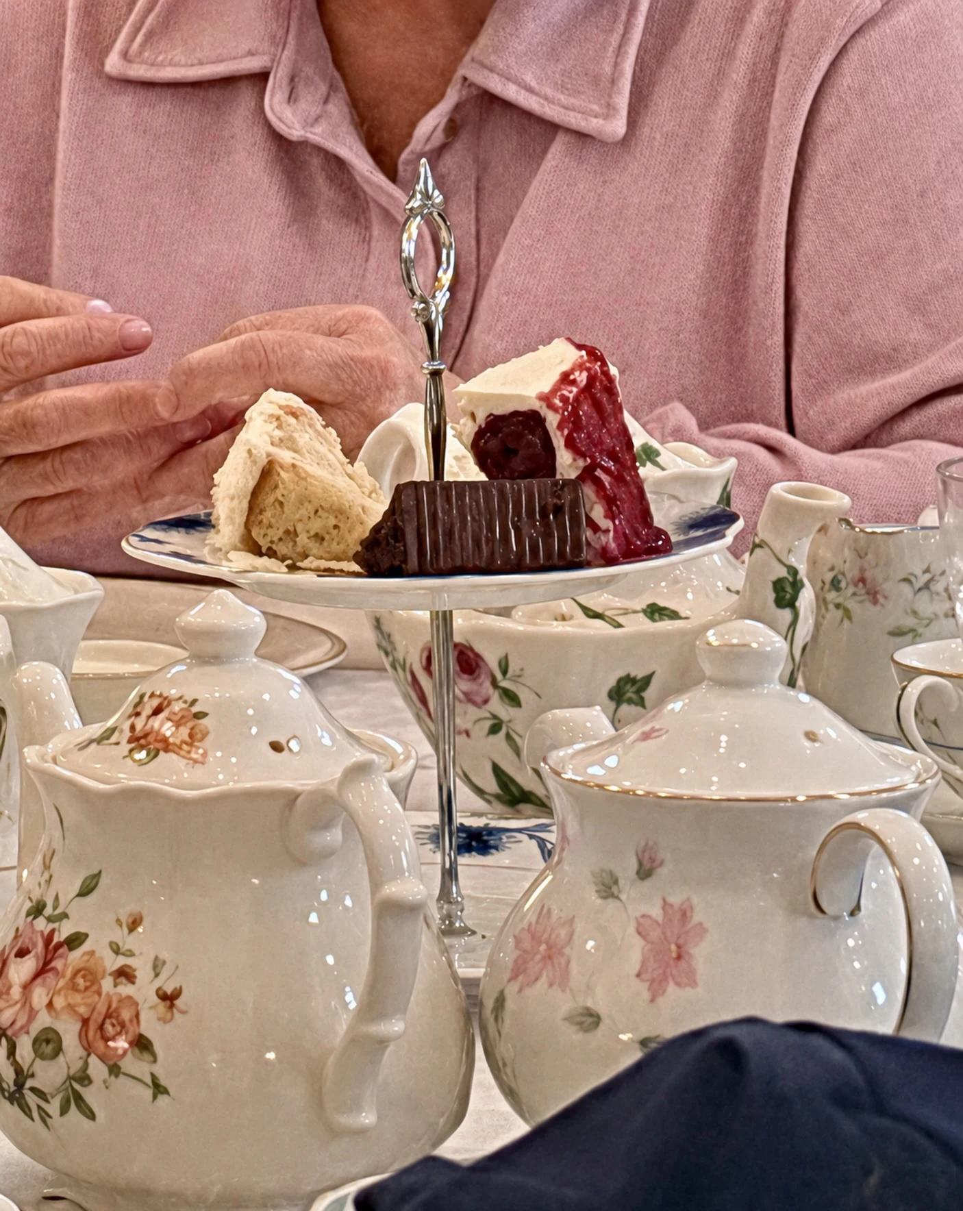 A guest enjoying tea beside floral china and a tiered pastry stand