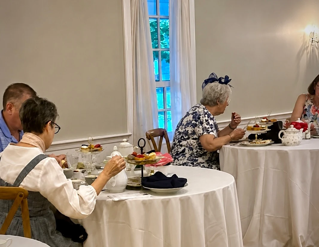 Guests sharing afternoon tea at linen-covered tables beside a tall window